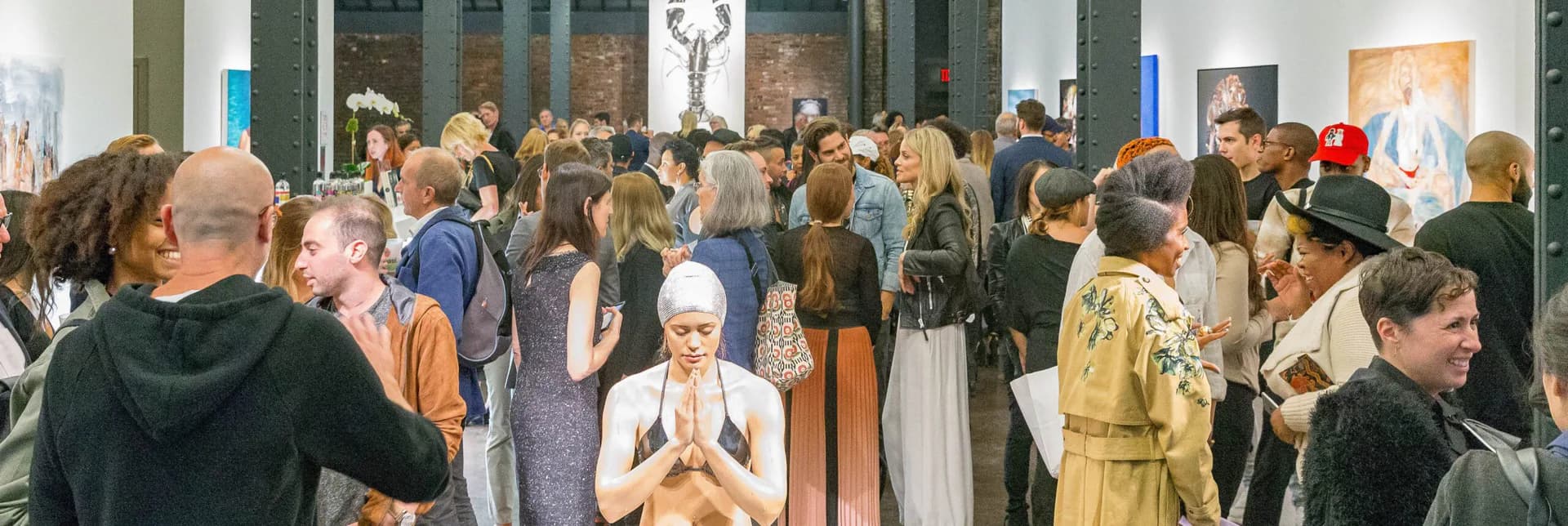Crowded gallery interior at Pen + Brush with diverse visitors in casual and formal attire viewing artwork on white walls.
