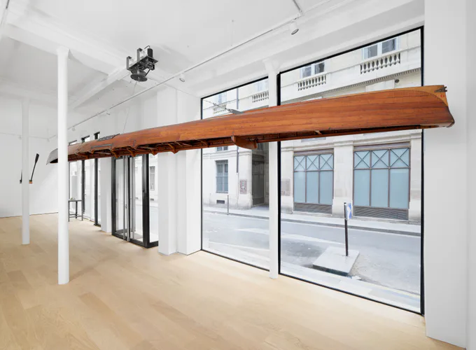 Interior of Peter Freeman, Inc. gallery showing white walls, wood beam soffit, large-frame glass doors opening to outdoor viewing area, and blonde wood flooring.
