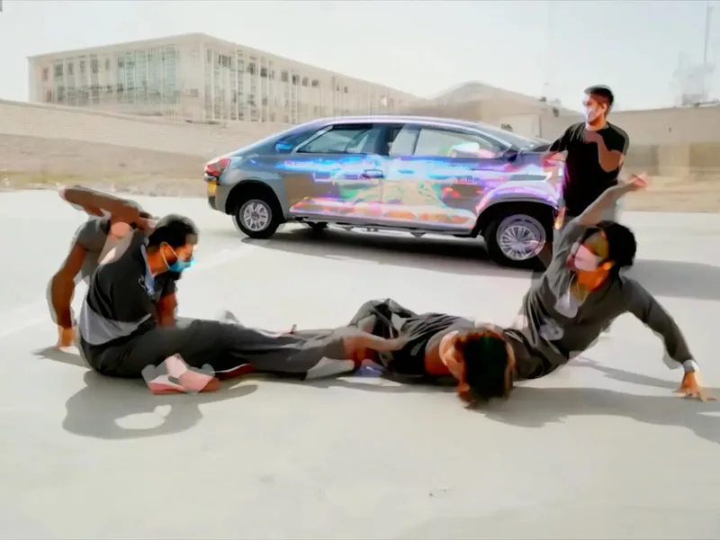 Installation artwork featuring a car wrapped in vibrant watercolor-style patterns with performers posing on white ground around the vehicle.