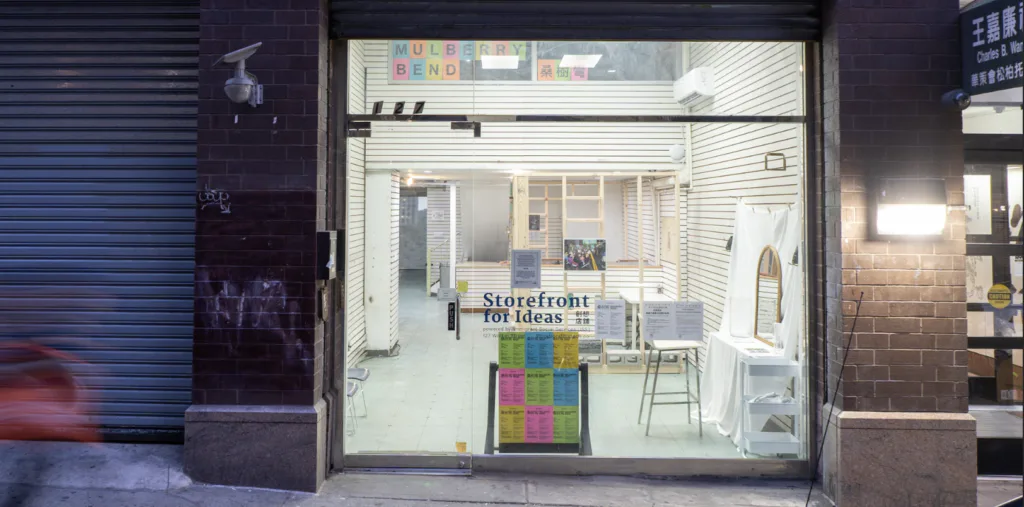 Storefront of PROTOCINEMA gallery at night, displaying a white interior with minimalist furnishings and colorful artwork visible through large glass facade.