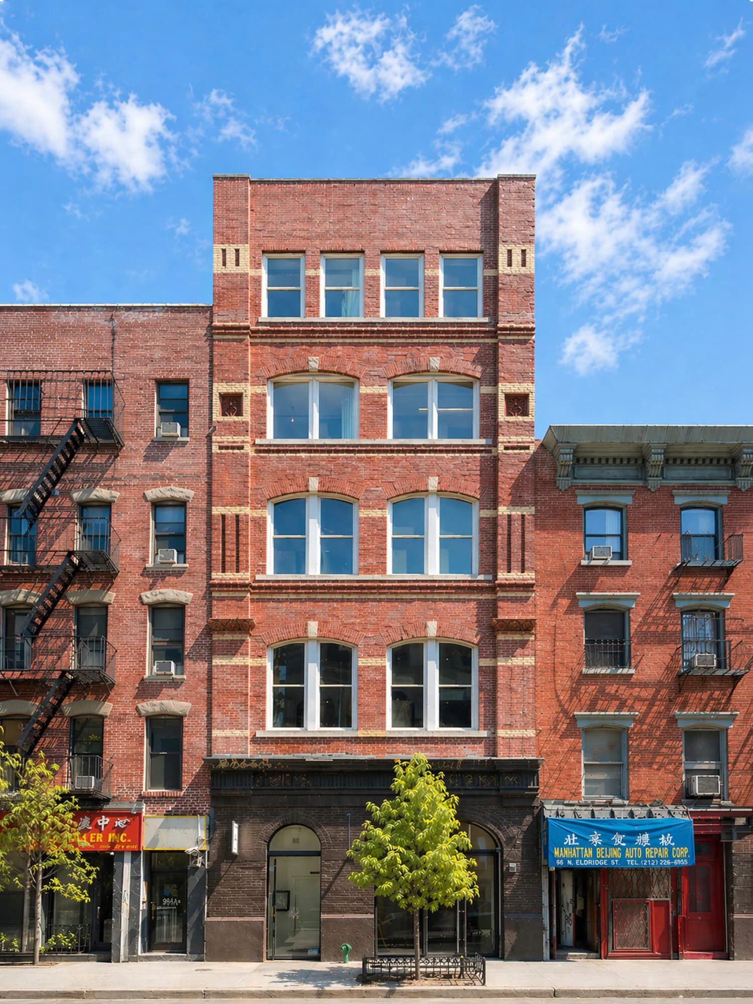 Exterior photograph of a brick building facade with large blue-framed windows, street-level storefronts, and clear blue sky above.