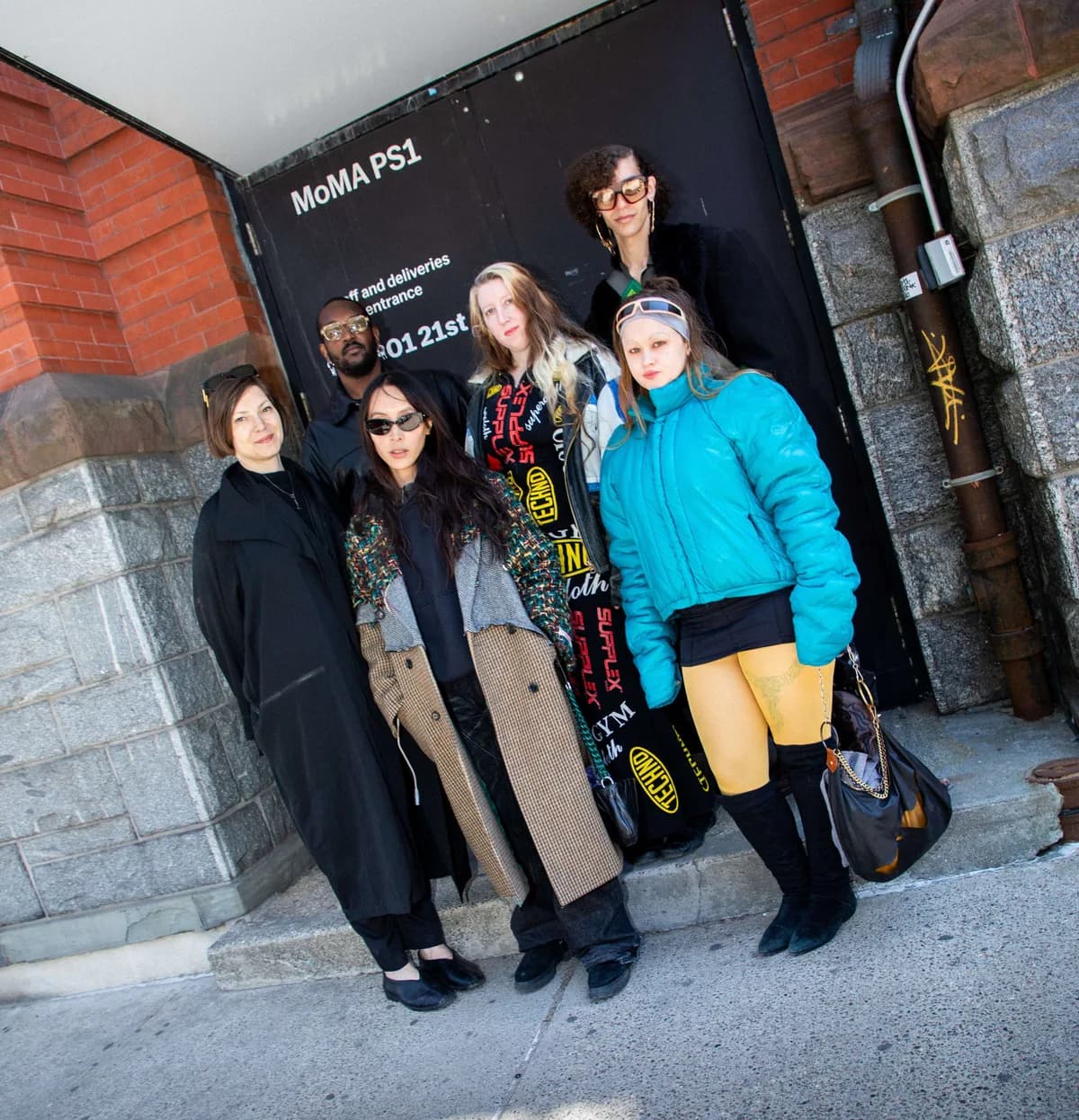 Five people posing together outside a building entrance with MoMA PS1 branding on dark signage above.