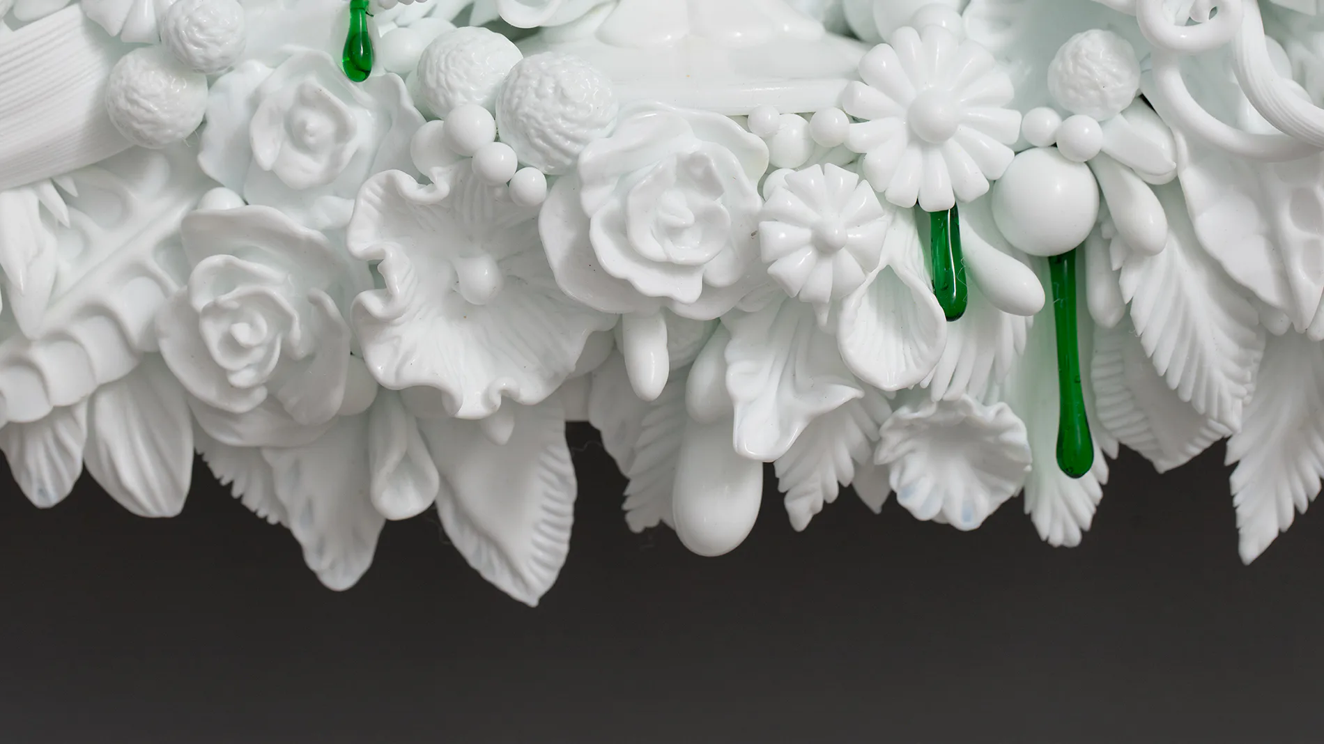 Cluster of white ceramic or plaster flowers with detailed petals and green stems hanging suspended against a dark background.