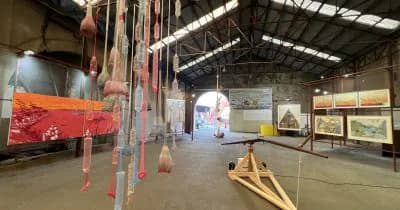 Industrial gallery interior at Residency Unlimited with red hanging textile installation, wooden geometric structures, and framed artworks on walls.