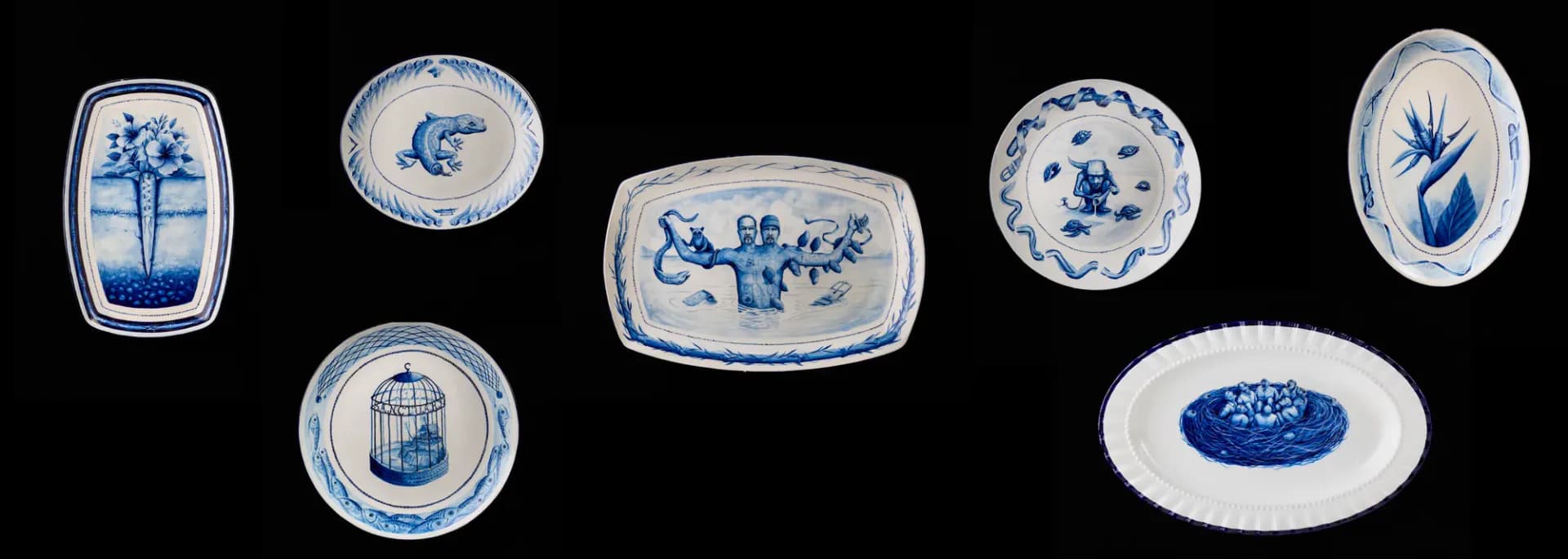 Collection of blue and white ceramic or porcelain dishes and plates arranged on black background, each featuring hand-painted decorative motifs including birds, flowers, and Asian-inspired designs.