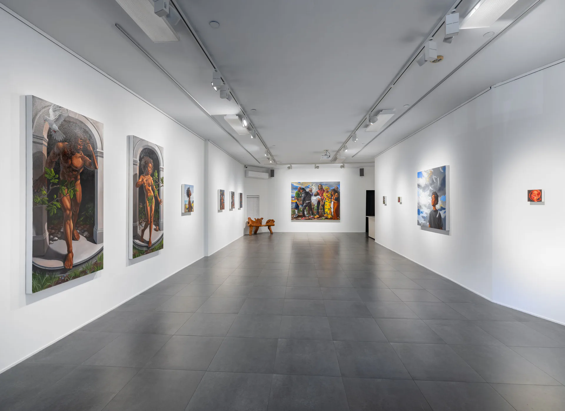 Gallery interior with polished gray floor, white walls, and large portrait paintings hung on both sides, visitors visible in the space.