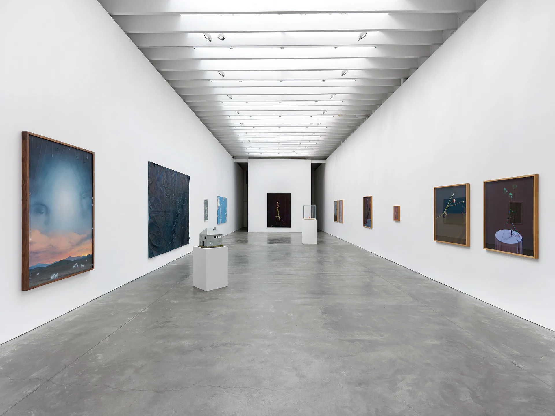 Contemporary gallery interior with polished concrete floor, white walls, track lighting, and several artworks displayed at intervals along the gallery walls.