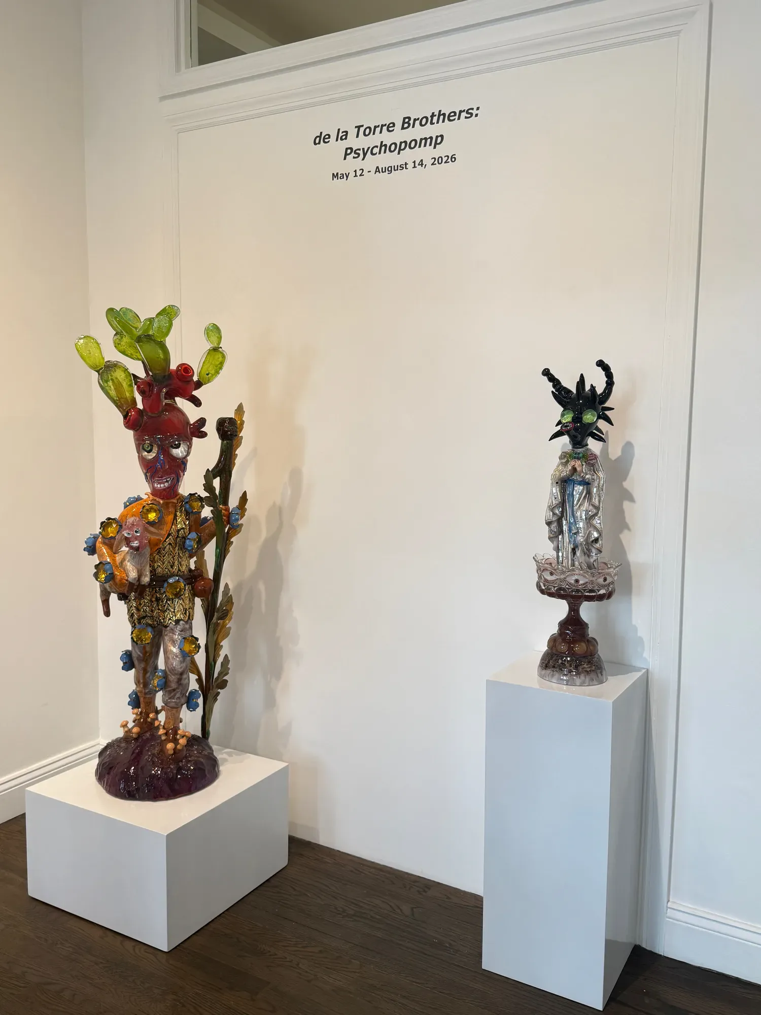 Gallery interior at Ruiz-Healy Art showing two tall sculptural works on white pedestals with exhibition text visible on wall.