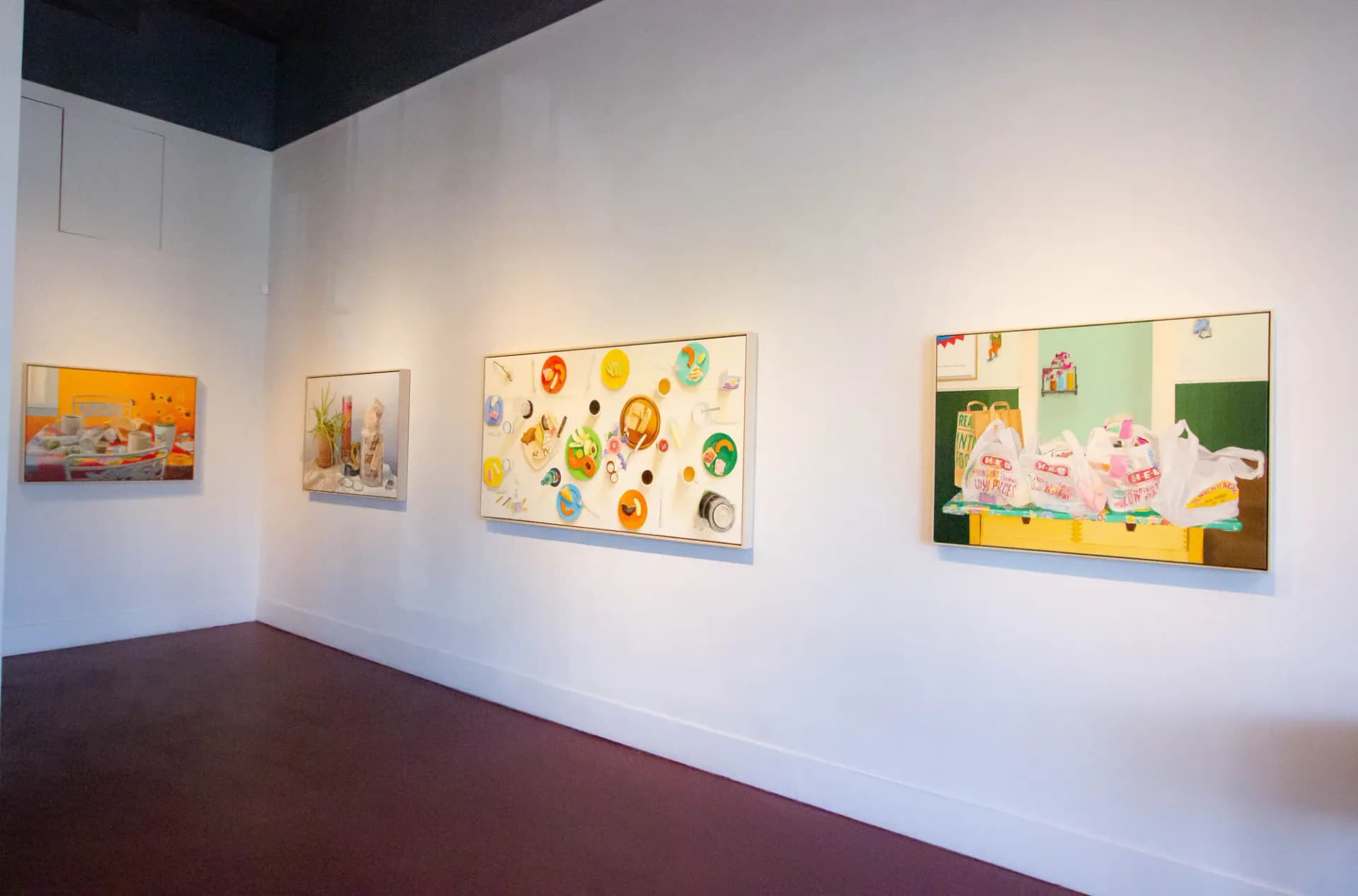 Gallery wall with three framed artworks displayed horizontally, featuring colorful compositions with organic and figurative imagery.