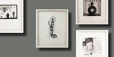 Gallery wall with gray background displaying five framed artworks of various sizes, including drawings, photographs, and a vinyl record image in black and white.