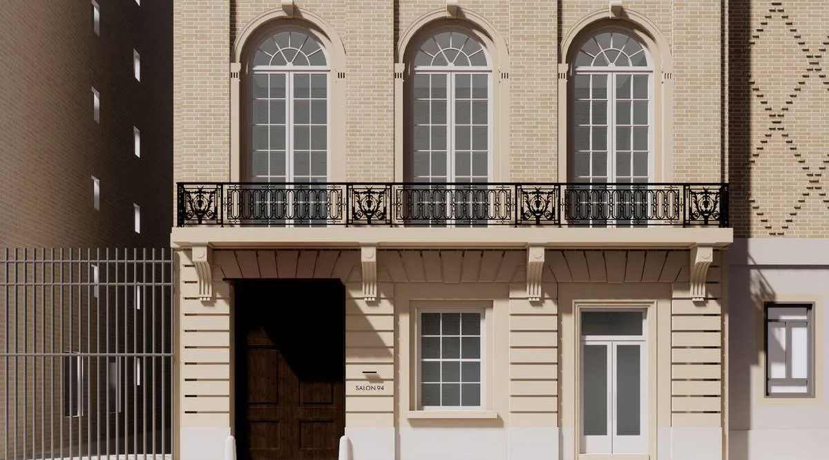 Neoclassical building facade with cream-colored brick, three arched windows with fanlight details on the upper floor, ornamental iron balcony, and dark wooden entrance door on the ground level.
