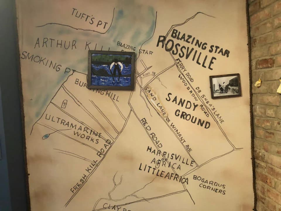 Hand-drawn map on beige paper showing Sandy Ground area of Staten Island with labeled locations including Blazing Star, Rossville, and Tufts Pt, with two small photographs pinned to the surface.
