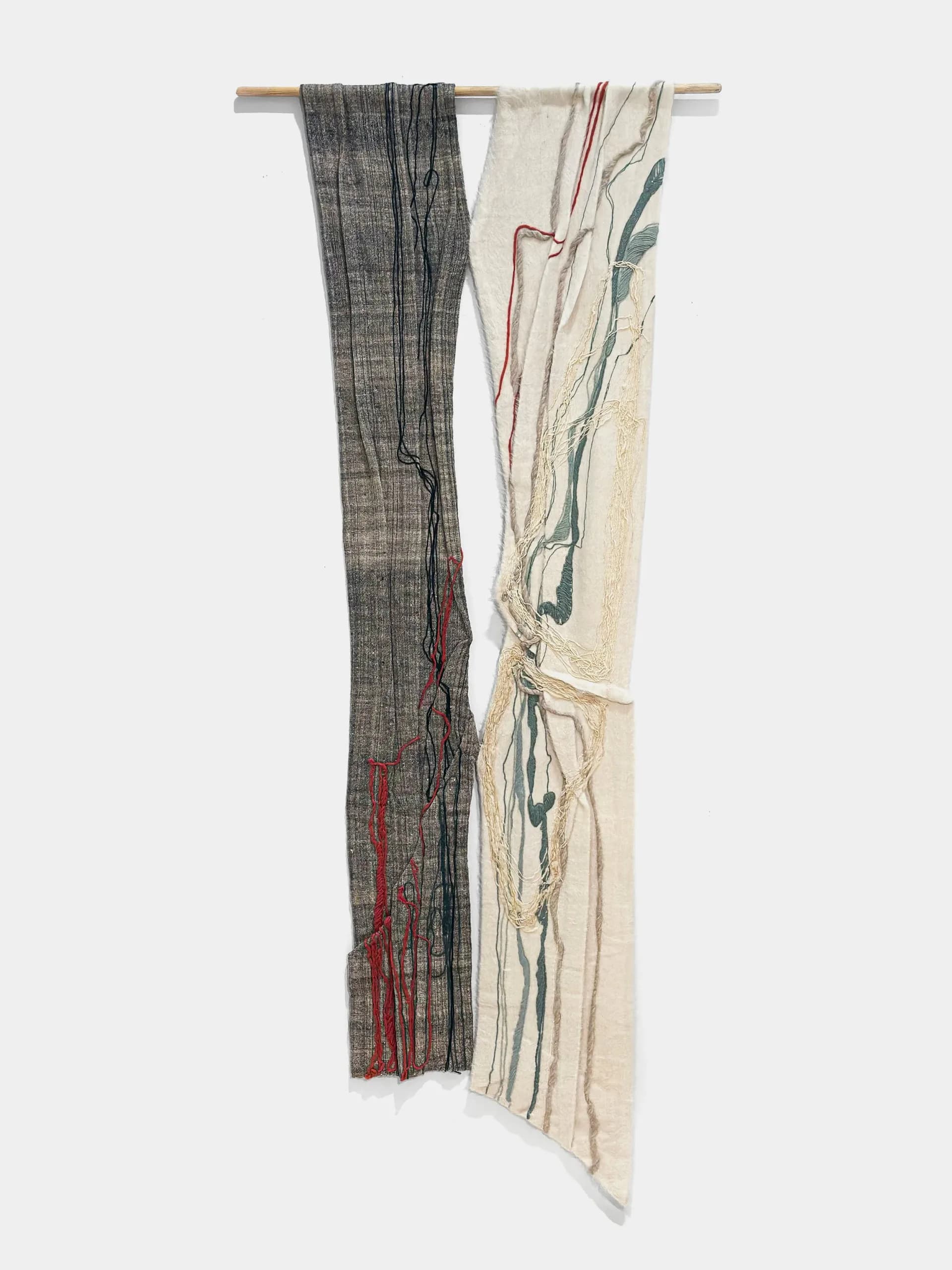 Two draped textile pieces hung on wooden rod: left side dark charcoal with red accents, right side cream with teal brushstroke-like marks.