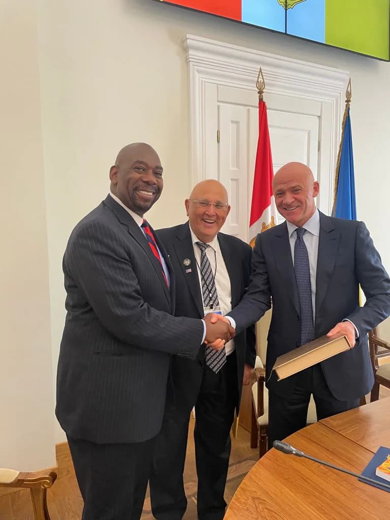 Three men in business suits shaking hands indoors with Polish and EU flags visible in background.