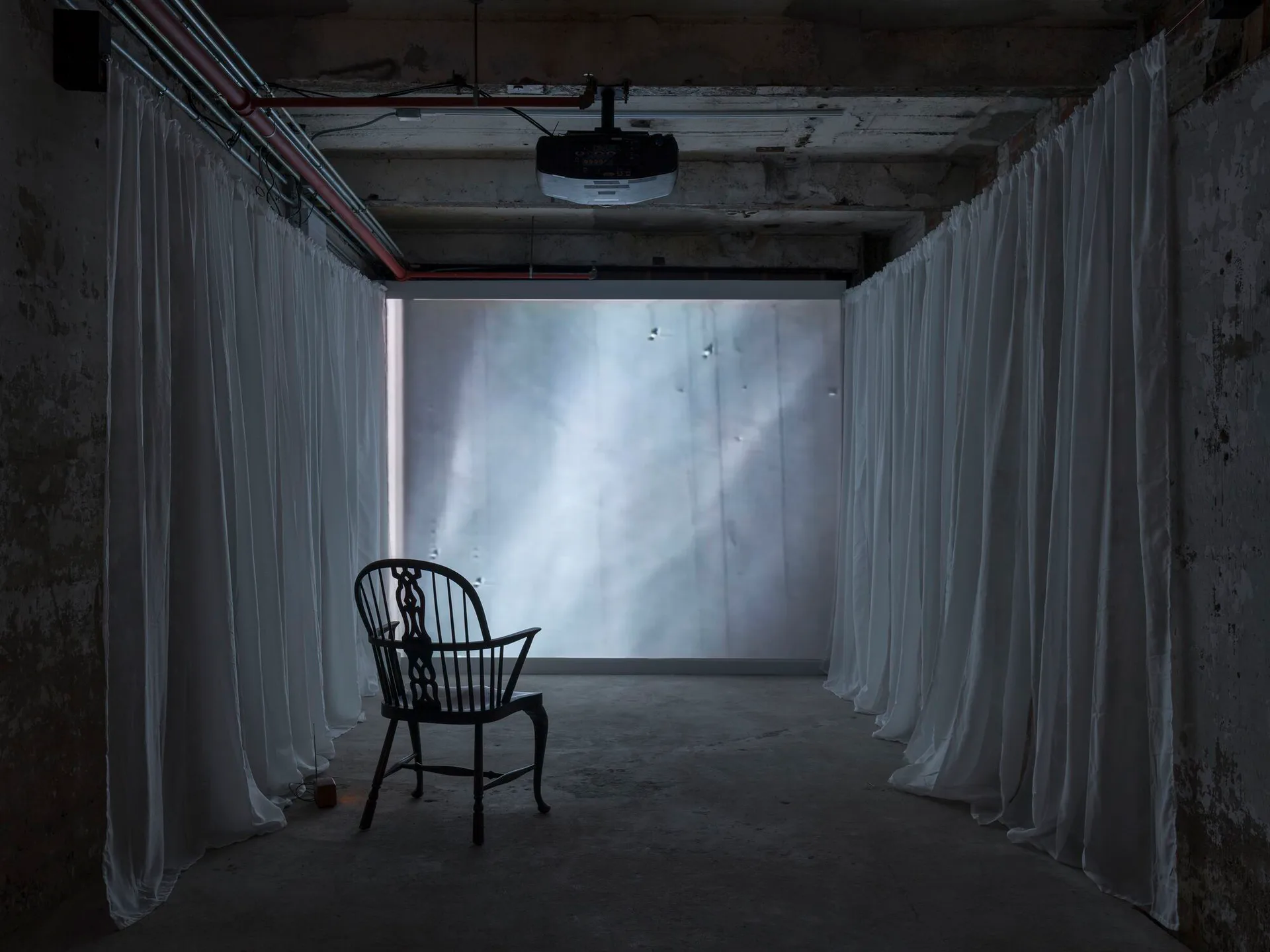 Interior installation with sheer white curtains framing window light, single black Windsor chair silhouetted in foreground.