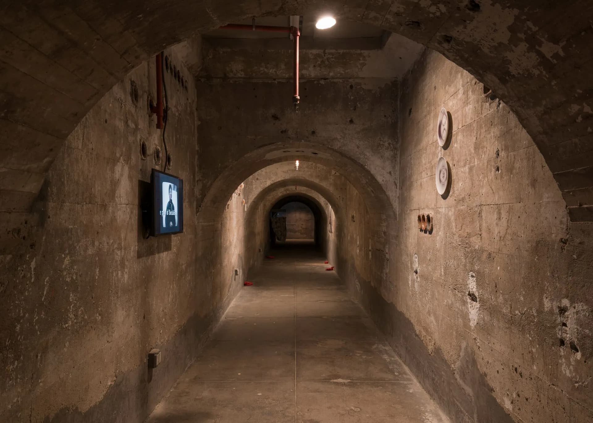 Underground tunnel corridor at SculptureCenter with barrel-vault concrete ceiling, receding arched openings, minimal lighting, raw industrial architectural space.