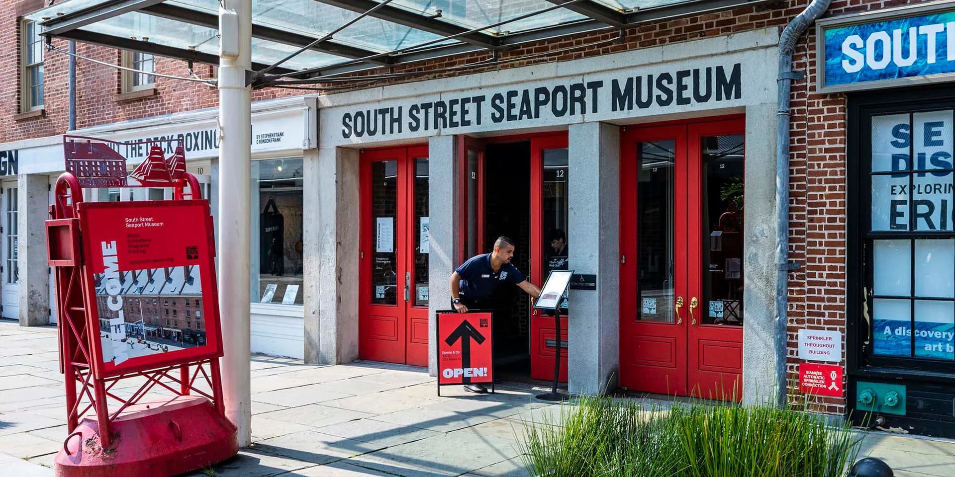 Exterior storefront of South Street Seaport Museum with red doors, glass windows, and signage on a brick building.
