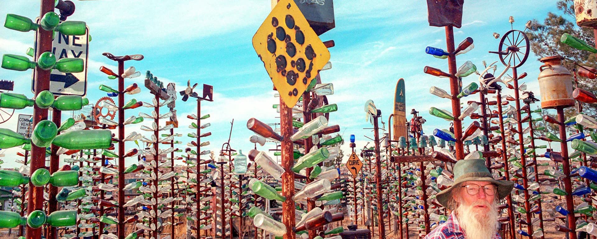 Colorful mixed-media installation featuring tall wooden structures decorated with objects, kites, and found materials against a bright sky.