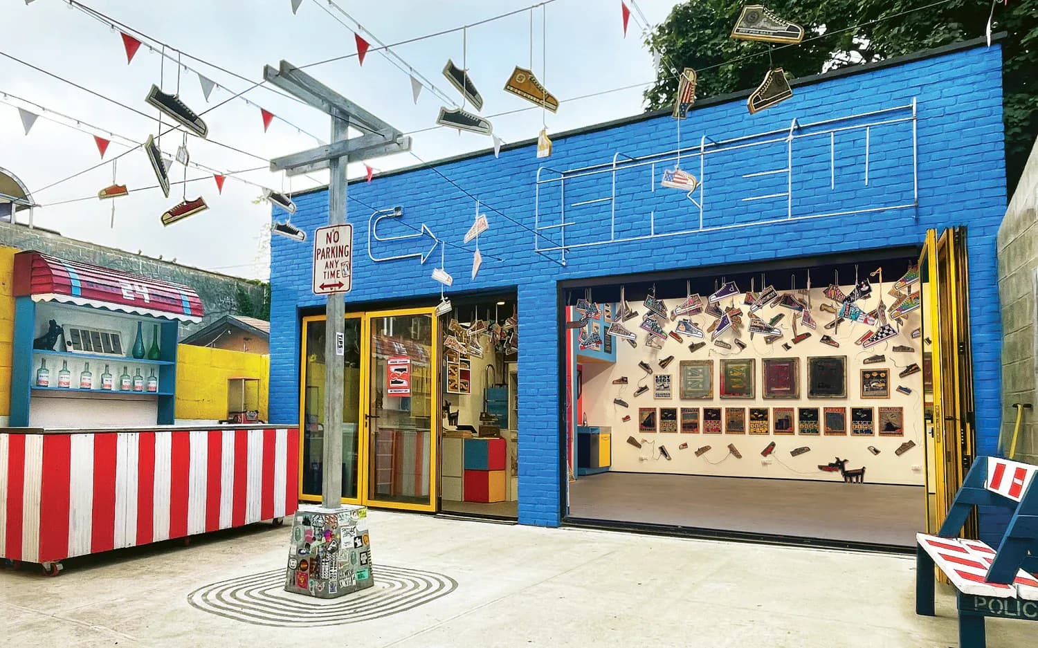 SKEWVILLE gallery exterior with blue facade, yellow-framed entrance, hanging sneakers, red and white striped stand, and interior artwork display visible.