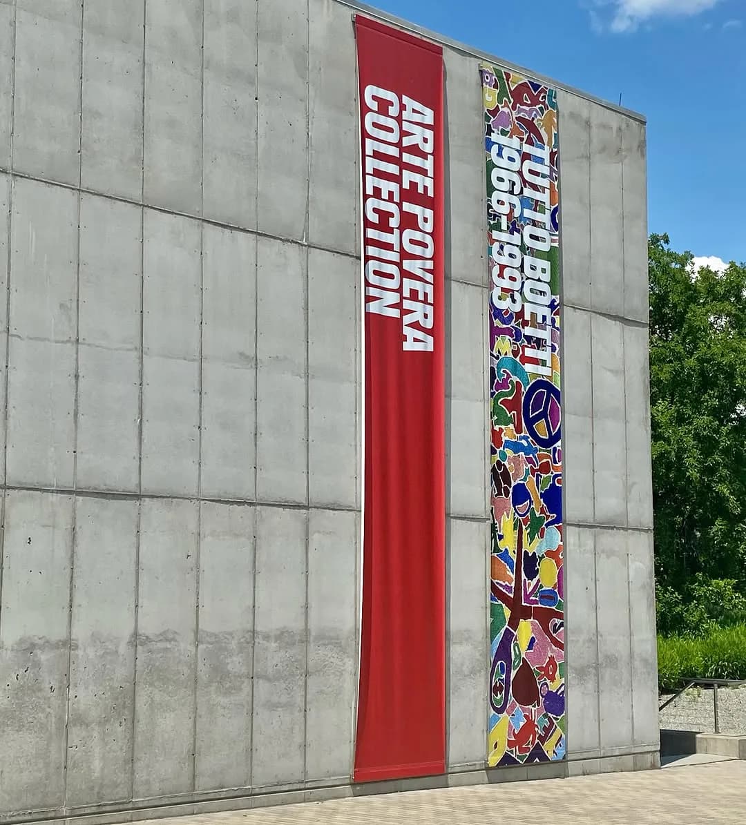 Exterior concrete wall with two large vertical banners—one red reading "ART POWER COLLECTION" and one colorful with abstract figures.