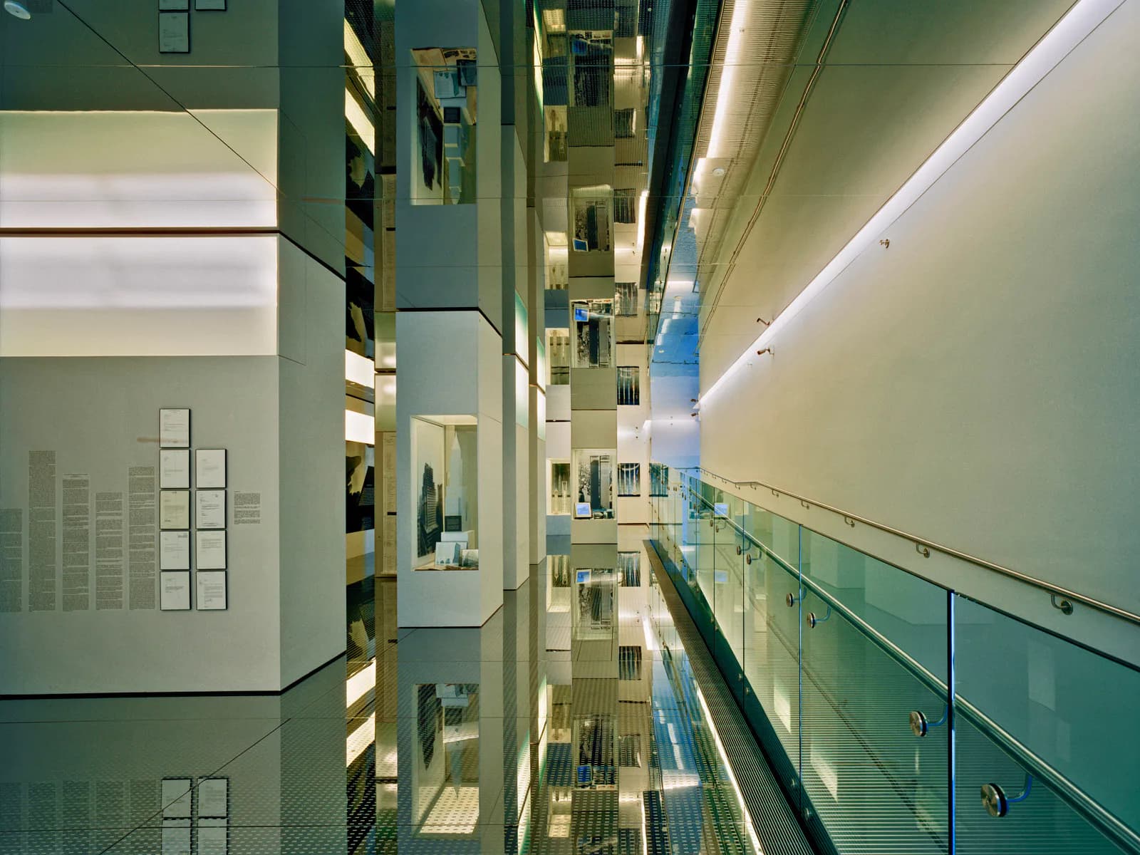 Interior of Skyscraper Museum gallery hallway with green walls, recessed lighting, glass railings, and architectural display panels mounted on walls.