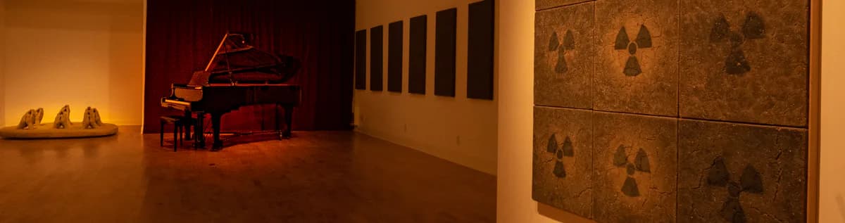 Soapbox Gallery interior with warm amber lighting, featuring a grand piano, wall-mounted sculptures, and textured panels with radiating patterns.