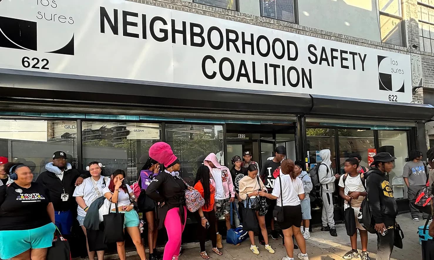 Exterior storefront photograph showing a sign reading 'NEIGHBORHOOD SAFETY COALITION' with people gathered outside at 622.