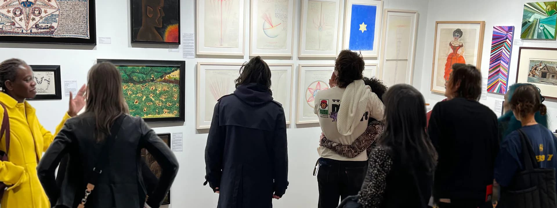 Gallery interior with visitors viewing framed artworks and photographs displayed on white walls.