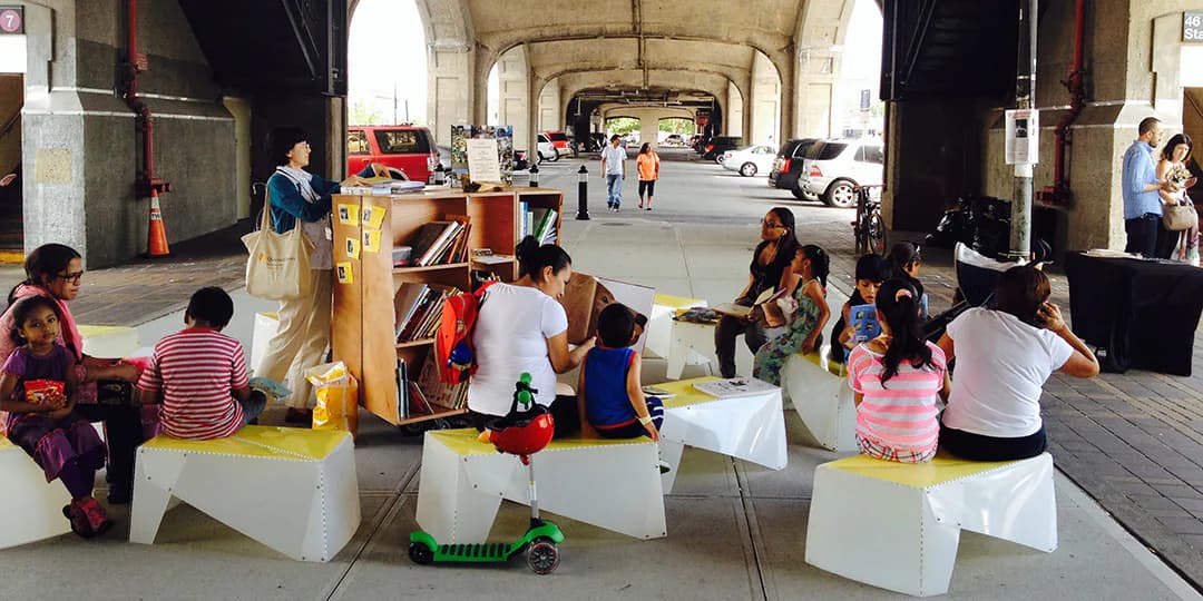 Children seated on white cubic platforms arranged in an arched corridor or underpass, appearing to be part of an interactive Street Lab installation.
