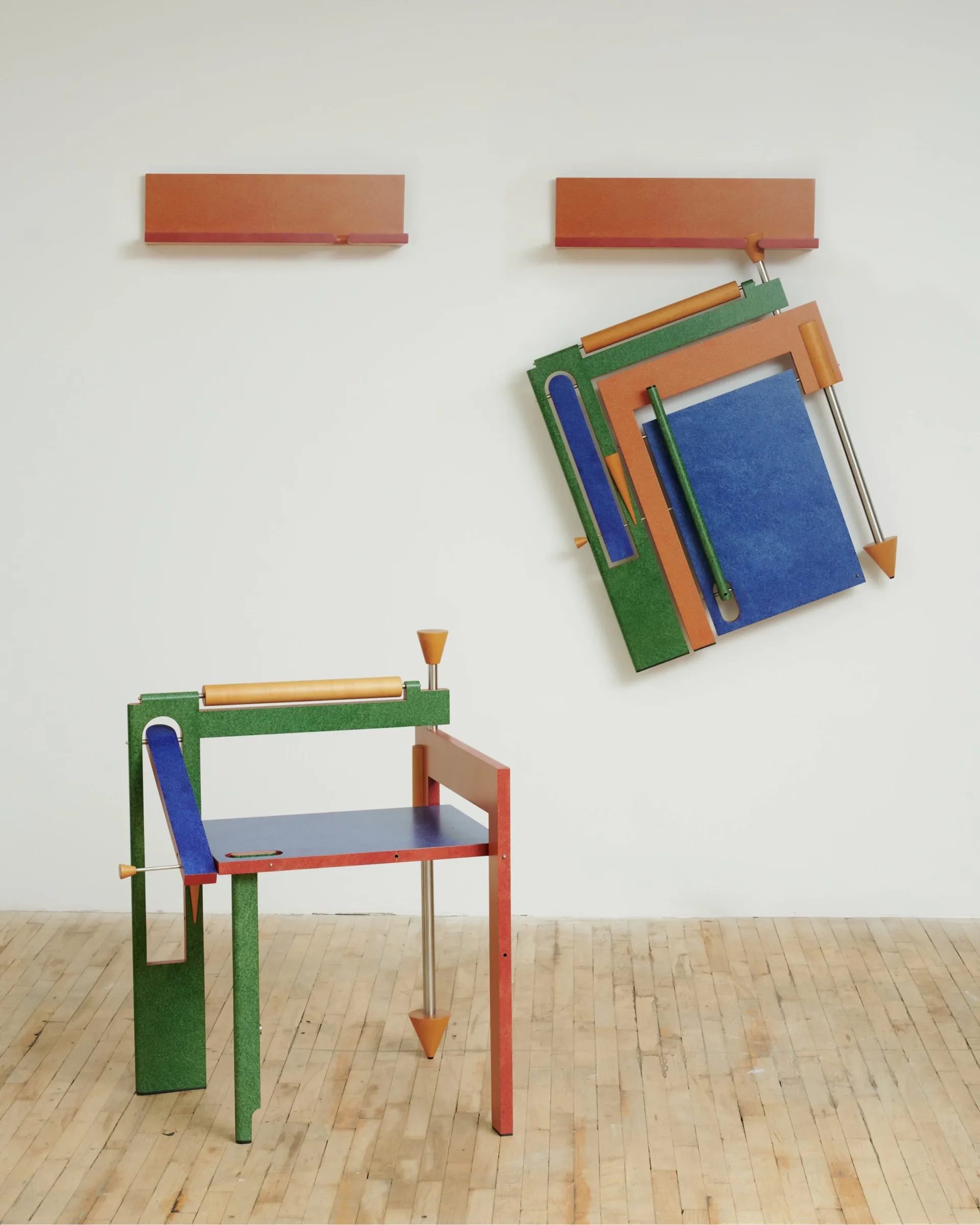 Mixed-media sculptural work: colorful wooden chair frames in green, red, and blue with geometric forms, plus suspended abstract wall pieces above.