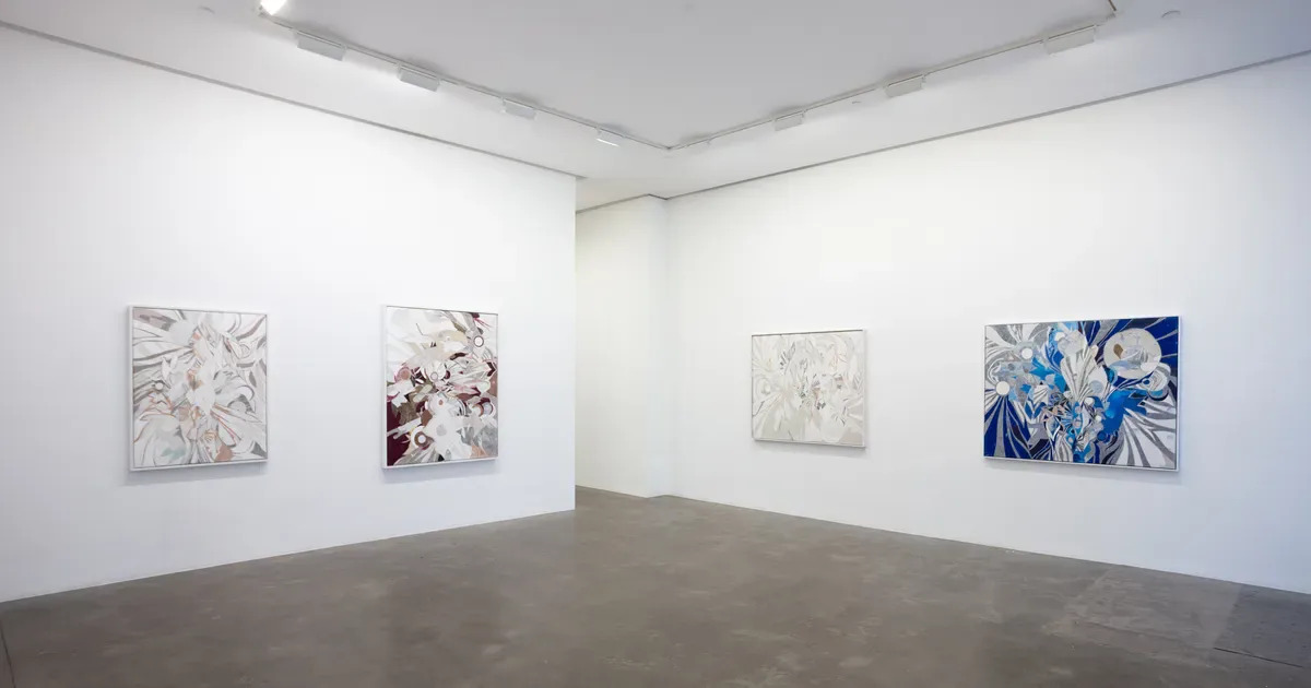 Minimalist gallery interior with four framed artworks on white walls, featuring abstract floral and botanical designs in muted and blue tones.