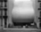Blurry grayscale photograph of cylindrical industrial vessel or tank beside a building structure.