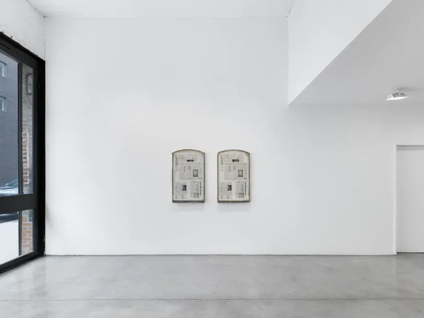 Minimalist gallery room with two small framed architectural drawings on white wall, black entrance door, and concrete flooring.