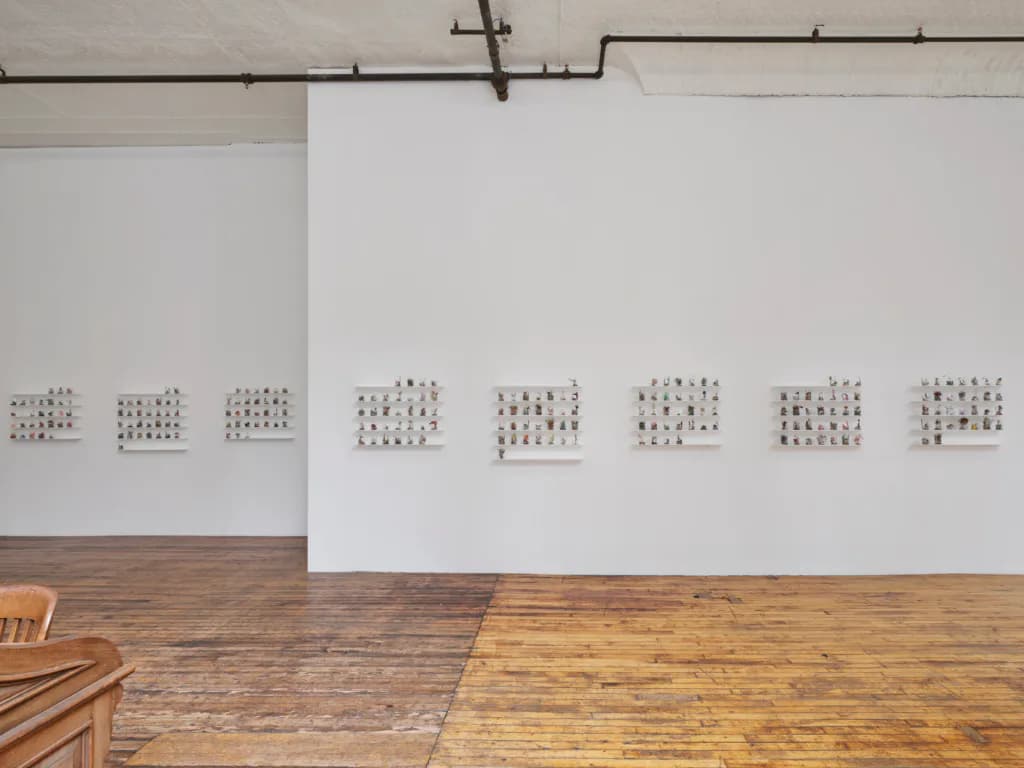 Gallery interior with eight small dot-pattern artworks mounted in a horizontal line across white walls above wooden flooring.