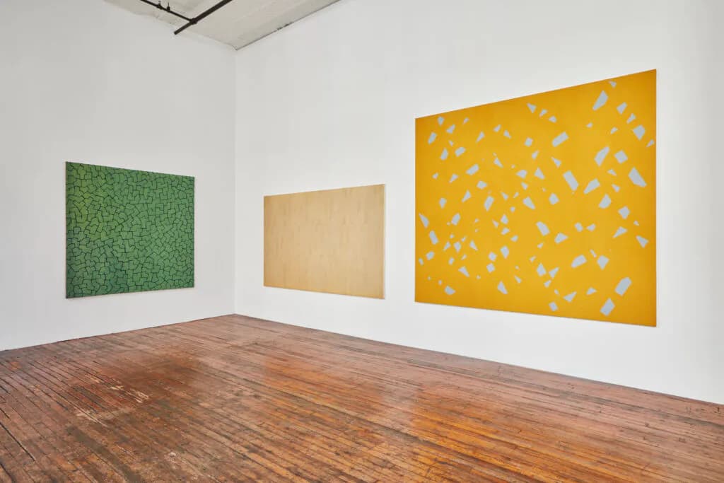 Gallery interior displaying three large abstract artworks: green textured canvas, tan minimal piece, and yellow composition with white scattered marks on white walls.