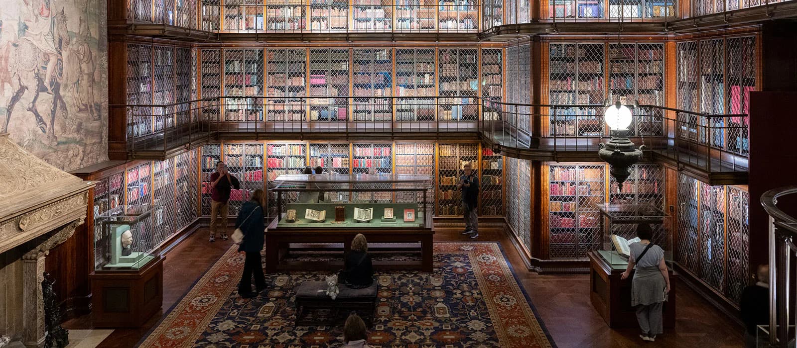 Interior of a historic library or manuscript room with wood-paneled walls, glass-fronted display cases containing books and documents, a central reading table, and ornate furnishings.