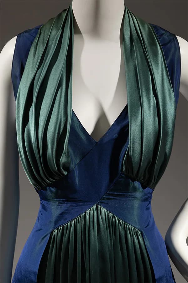 Navy blue sleeveless wrap dress with gathered green scarves draped from neckline, displayed on dress form.