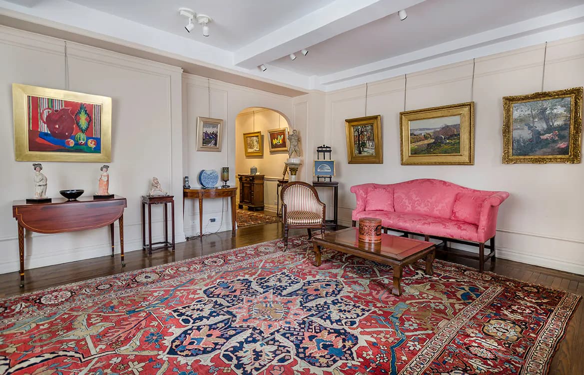 Gallery interior with pink sofa, patterned rug, wooden side tables, and paintings hung on white walls