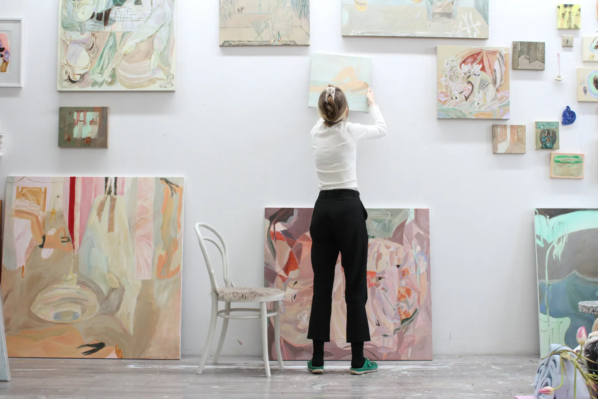Gallery interior at Triangle showing a person viewing paintings and drawings pinned to white walls, with a chair and sculptural elements visible.