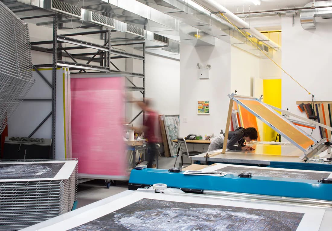 Print studio interior at Two Palms with screen printing equipment, metal shelving, and a person working at a press
