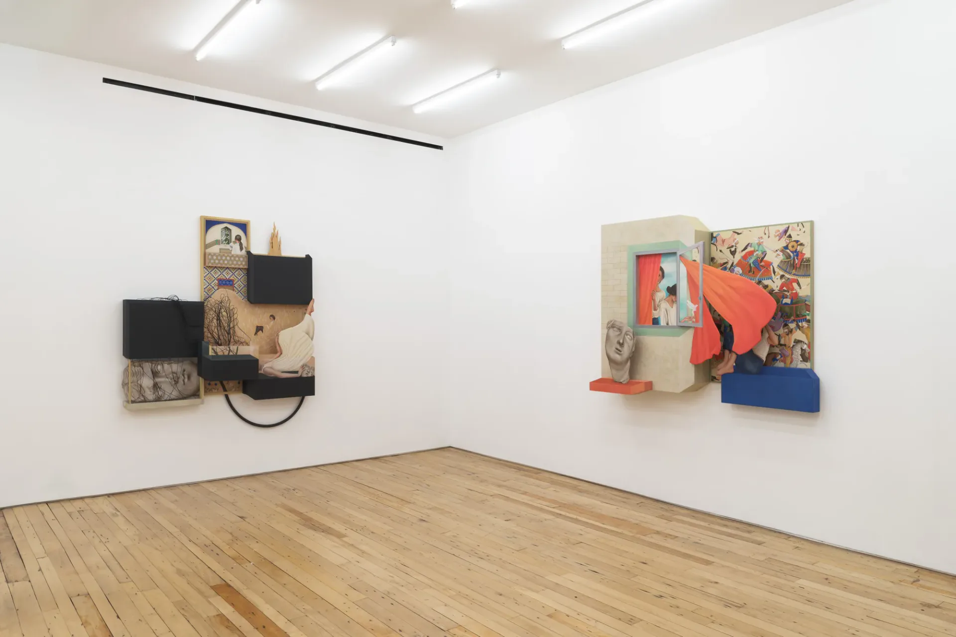 Gallery with wooden floor displaying two mixed-media wall installations: one with black elements on left, one with colorful forms and blue base on right.
