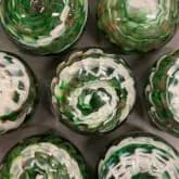 Six glass vessels with spiral green and white decorative patterns arranged on dark surface.
