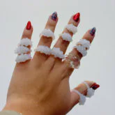 Hand wearing five sculptural glass rings in translucent white and red, displayed against neutral background.