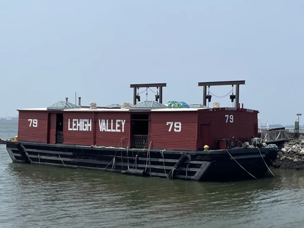 Red and black industrial barge numbered 79 labeled 'Lehigh Valley' moored on muddy waterfront with industrial structures visible.