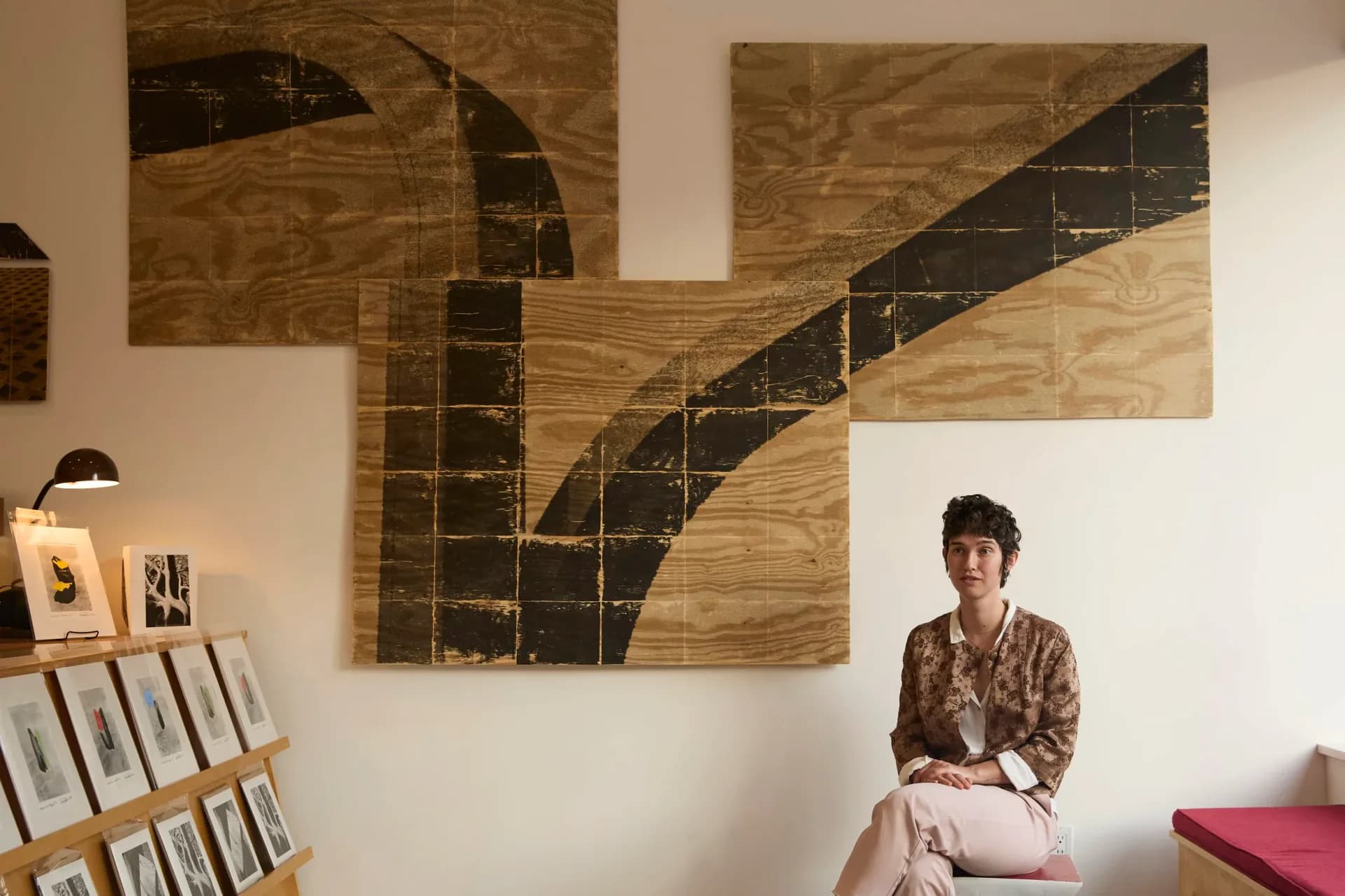 Interior photograph of Westlab + Gallery showing wood and black geometric wall artwork, person sitting on pink bench, and publication displays on left wall.