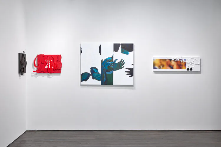 Gallery wall with white background displaying five artworks of varying sizes: abstract red form, blue and teal mixed-media piece, black and white composition with hands, and orange/warm-toned artwork.