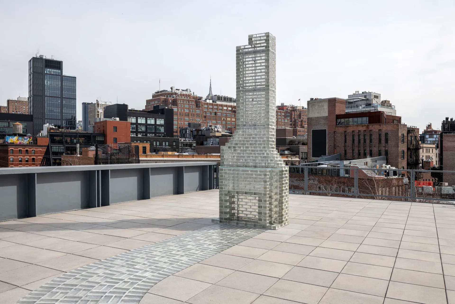 Photograph of a rooftop terrace with pale green brick chimney structure, overlooking Manhattan's Lower East Side skyline.
