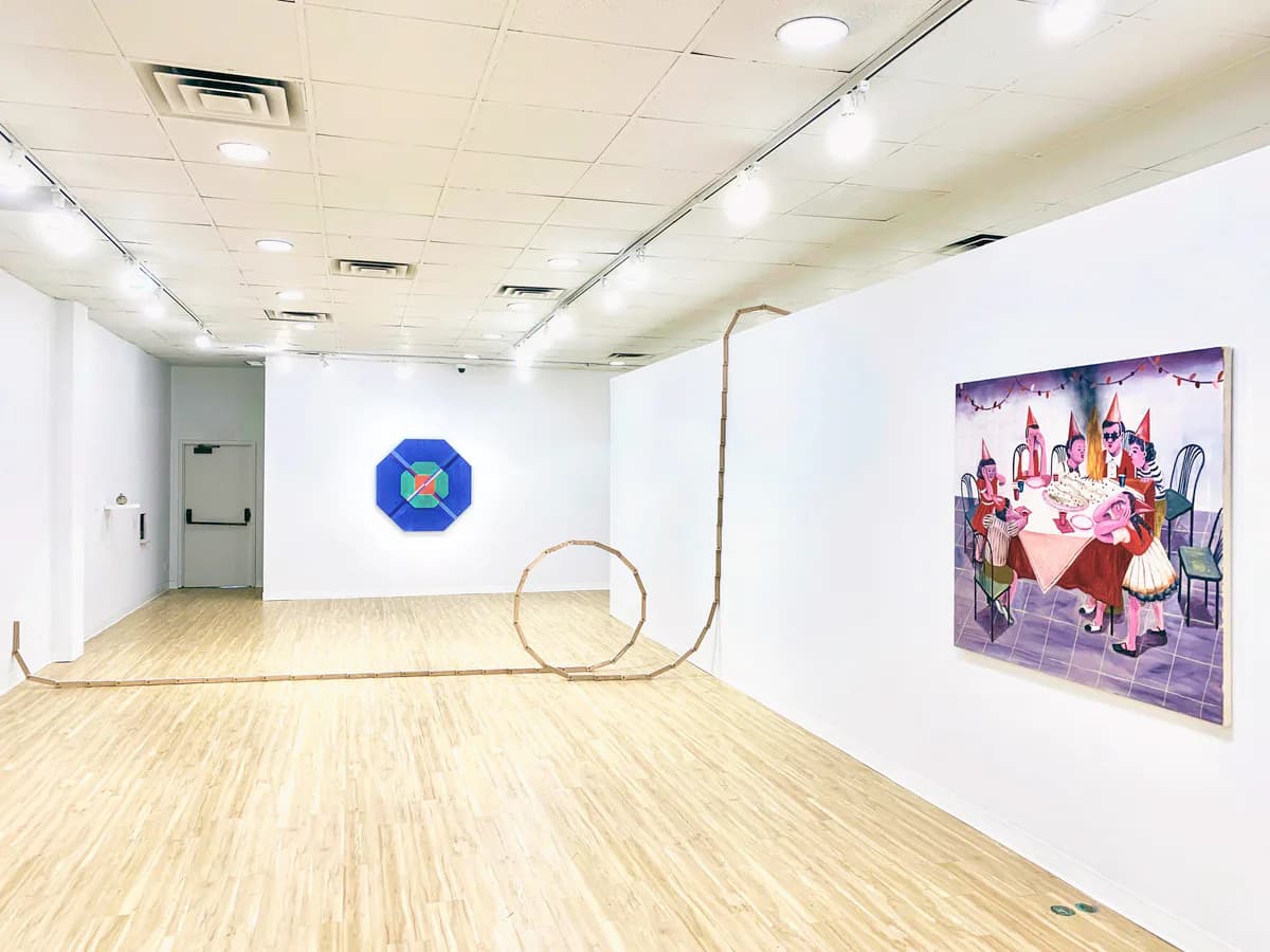 Interior of Yeh Art Gallery with white walls, wood floor, track lighting, a wall-mounted geometric sculpture, a sculptural wooden loop on the floor, and a colorful figurative painting on the right wall