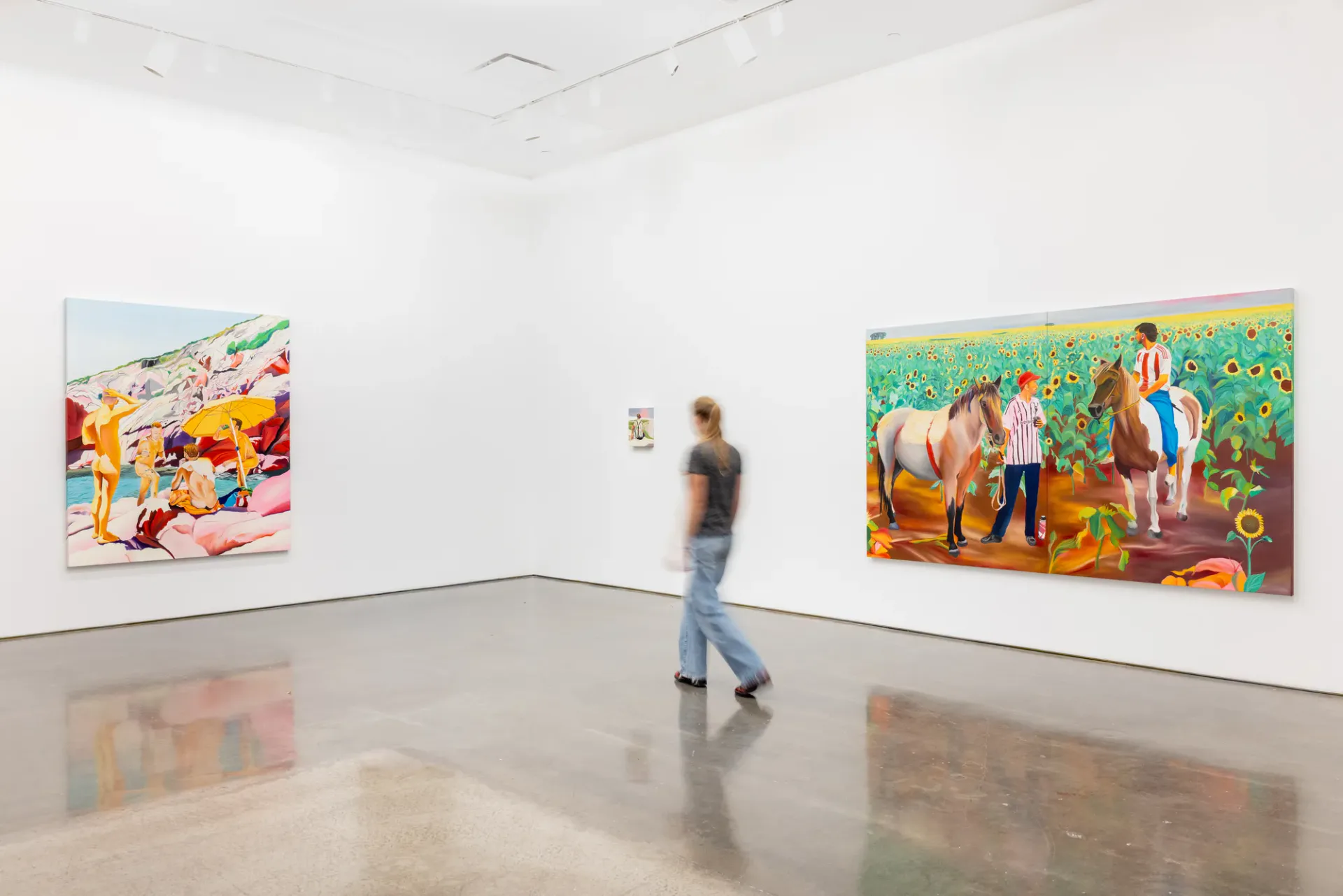 A gallery visitor in jeans walks through a bright, minimalist white gallery space with reflective floors and large colorful artworks on the walls.