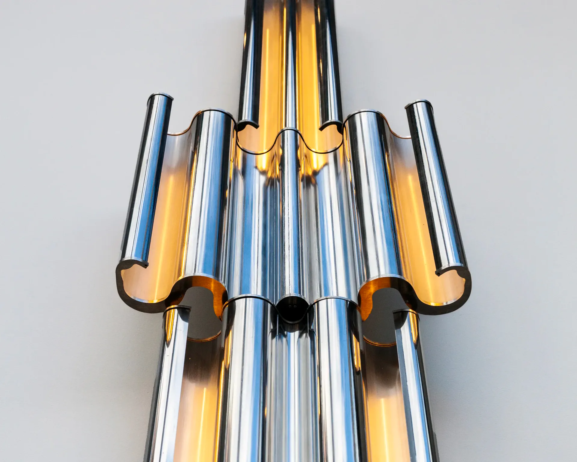 An abstract sculptural artwork featuring chrome cylindrical tubes with blue and gold striping, arranged vertically with organic cutout forms.